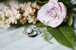 engagement ring and wedding bands photgraphed with a light pink rose on a white cloth