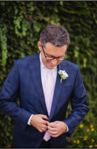 A groom or man buttoning his navy suit, looking down and smiling