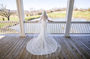 Bride with long train standing on a porch overlooking farm 