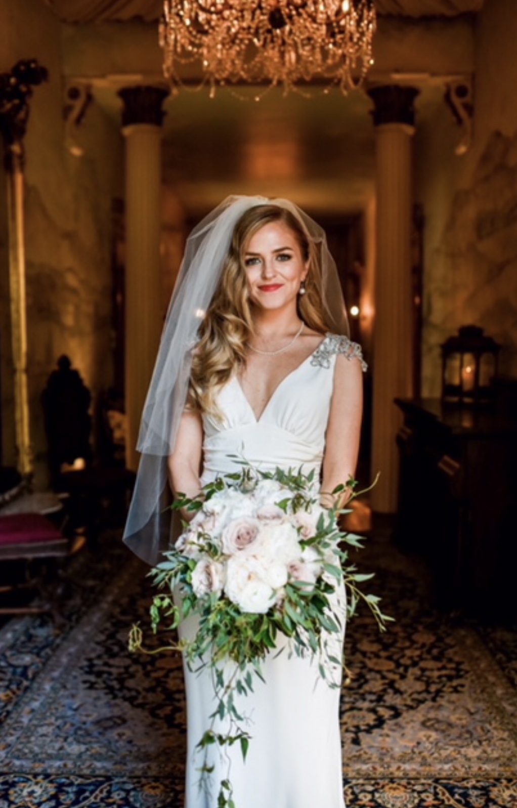 Bride with deep vintage waves, side part, red lipstick, bouquet and veil smiling at the camera